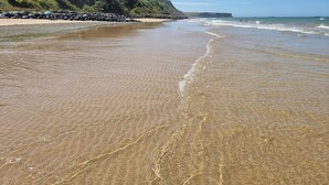 A beach with clear shallow waters, a rocky shoreline, and a grassy cliff. - La Bayeuzen - Cabane Balnéo Panoramic sea view - Normandie Arromanches (Saint-Côme-de-Fresné)