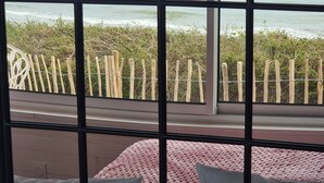 A room with a large window overlooking a beach and the sea. There is a bed with white pillows and a pink blanket. - La Bayeuzen - Cabane Balnéo Panoramic sea view - Normandie Arromanches (Saint-Côme-de-Fresné)