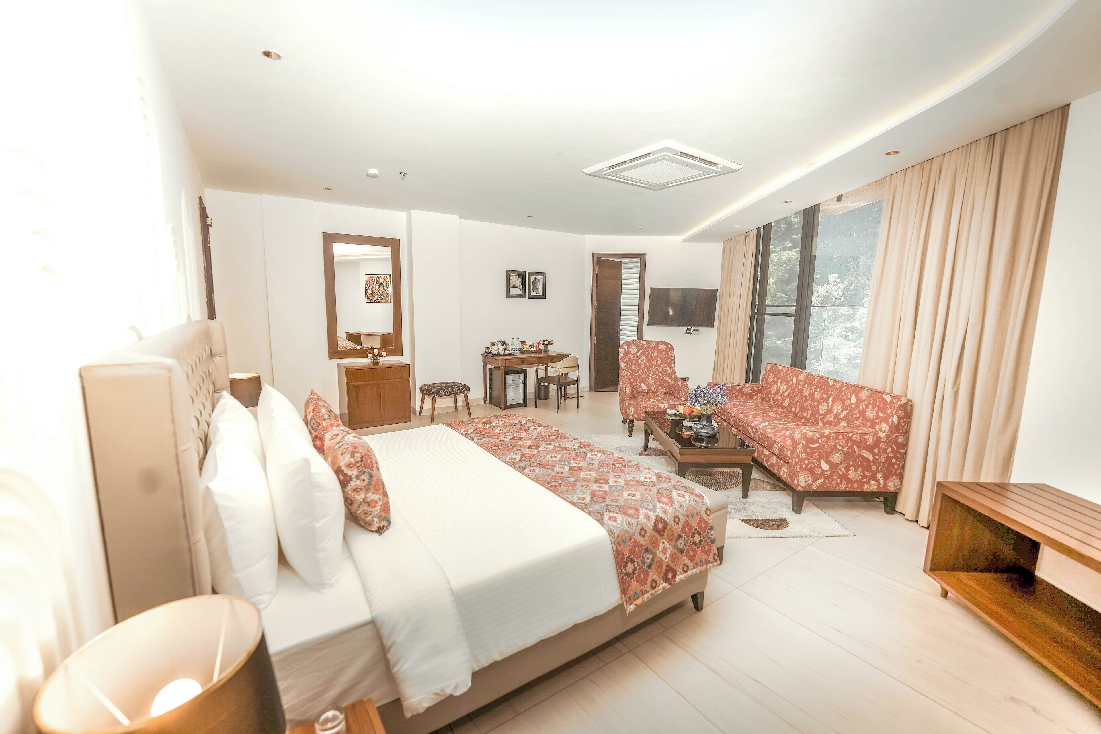A modern hotel room with a large bed, a sofa, a desk, and a TV.