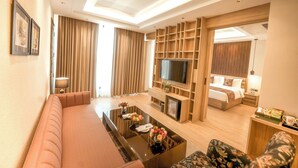 A modern hotel room with a sofa, a coffee table with flowers, a TV, a bed, and a nightstand. - NAMAMI BY ZENQ BANKHANDI (Dera Gopipur)