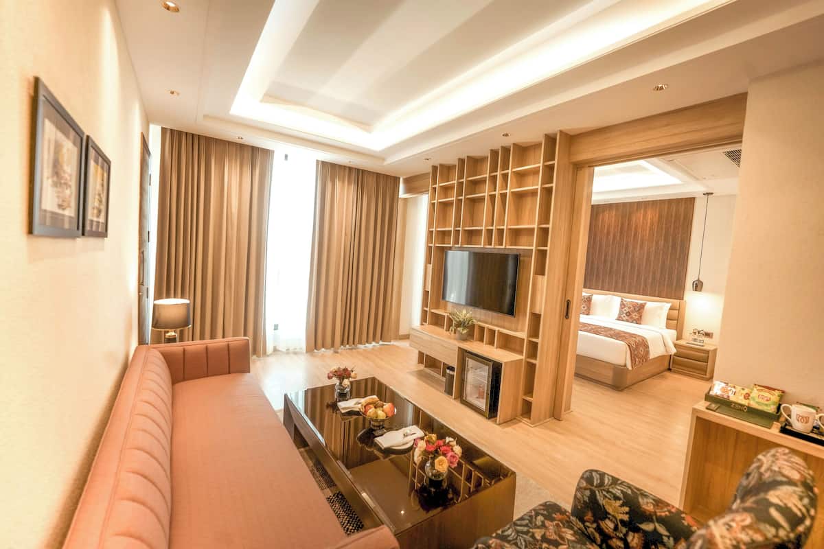 Quarto de hotel moderno com sofá, mesa de centro com flores, televisão, cama e mesa de cabeceira.