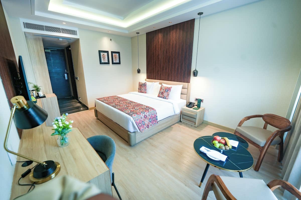 Quarto de hotel moderno com cama grande, mesa de cabeceira, escrivaninha e área de estar.