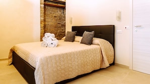 Una cama bien hecha con colcha color beige, dos almohadas y toallas enrolladas a un lado.