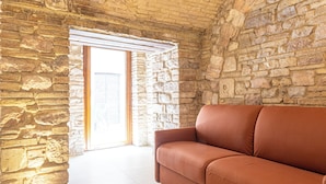 Una habitación con pared de piedra, un sofá de cuero marrón y una puerta que da al exterior.