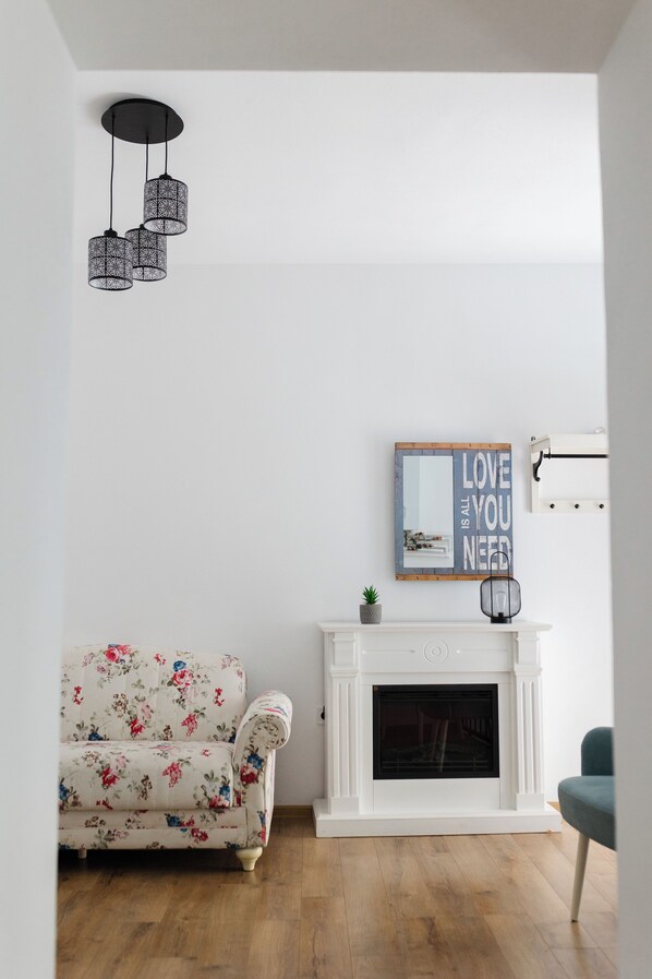Una sala de estar con chimenea blanca, un sofá floral y una lámpara colgante.