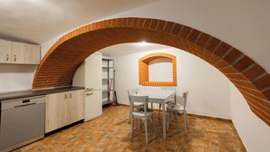 Una cocina con arco de ladrillo, armarios blancos y comedor con mesa y sillas.