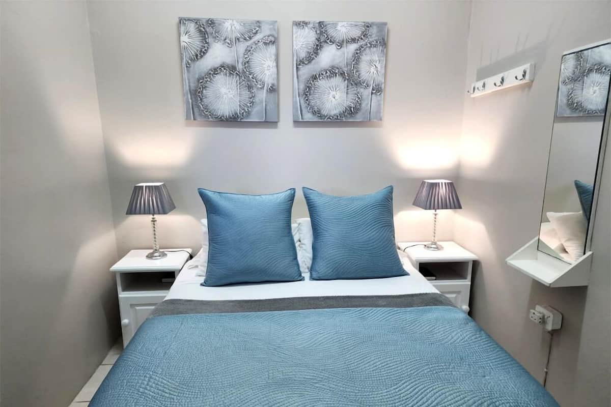 A modern bedroom with a large bed, two bedside tables with lamps, and two wall-mounted artwork pieces.