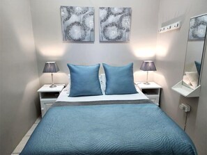 A modern bedroom with a large bed, two bedside tables with lamps, and two wall-mounted artwork pieces. - Muir Holiday Apartments (Still Bay)