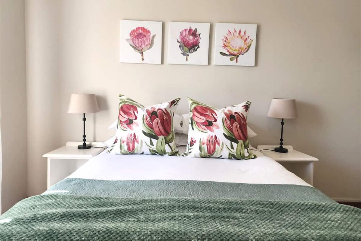 A bedroom with a bed, two nightstands, three wall-mounted floral paintings, and two lamps.