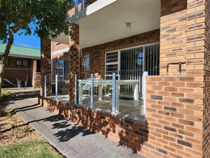 A brick building with a covered patio area featuring a table and chairs. - Muir Holiday Apartments (Still Bay)