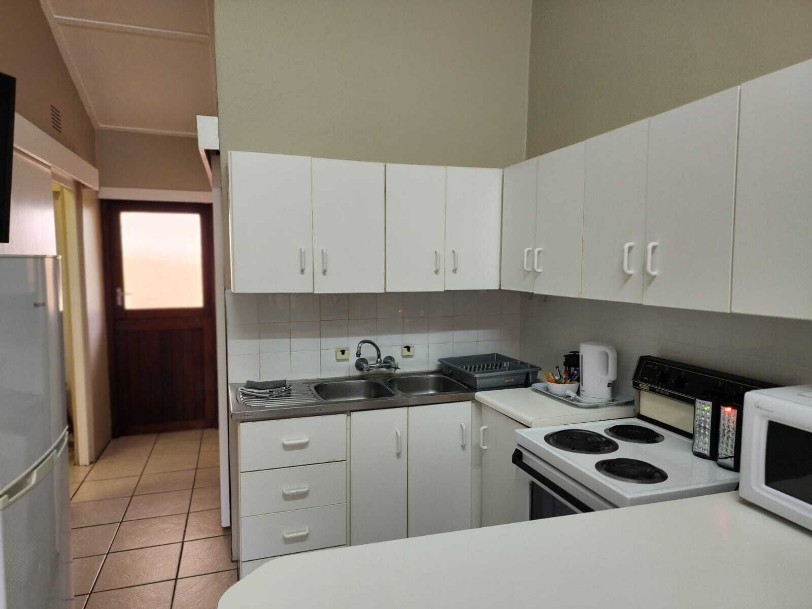 A compact kitchen with white cabinets, a stainless steel sink, a stove, and a microwave.
