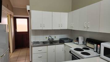 A compact kitchen with white cabinets, a stainless steel sink, a stove, and a microwave.