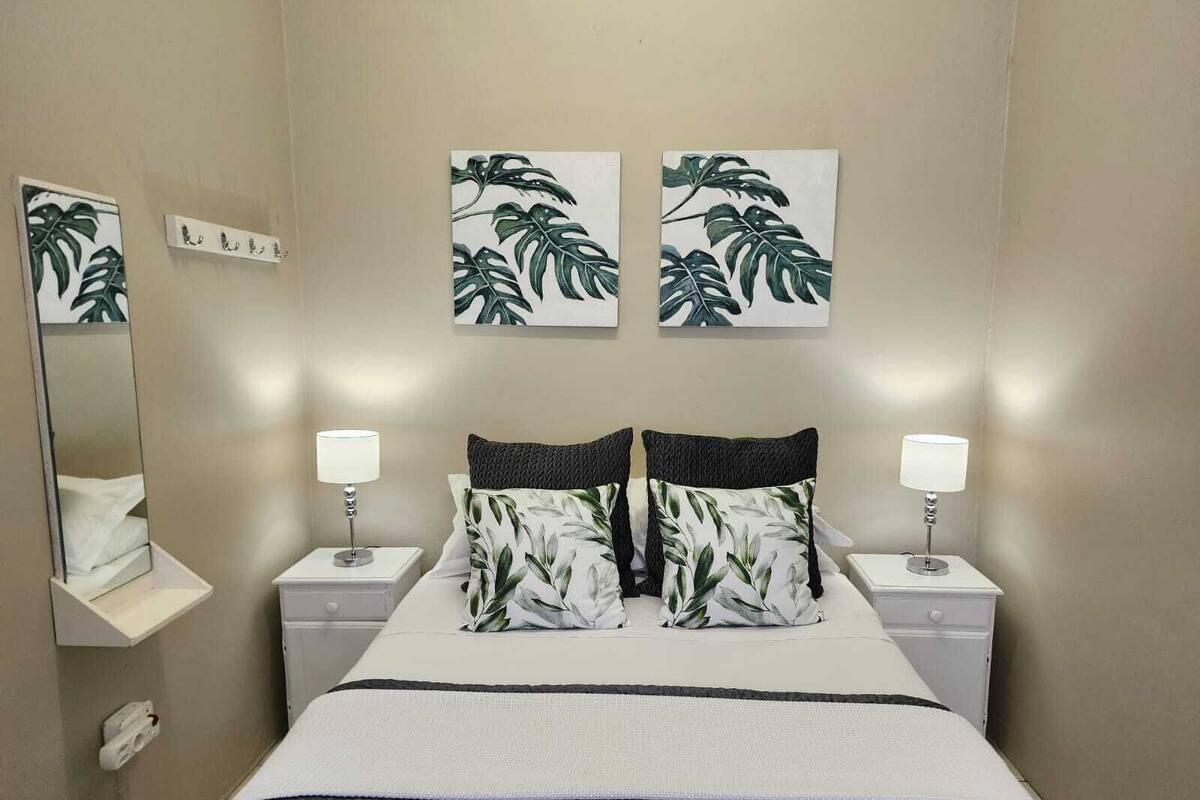 A neatly arranged bedroom with a bed, two nightstands, a mirror, and wall art.