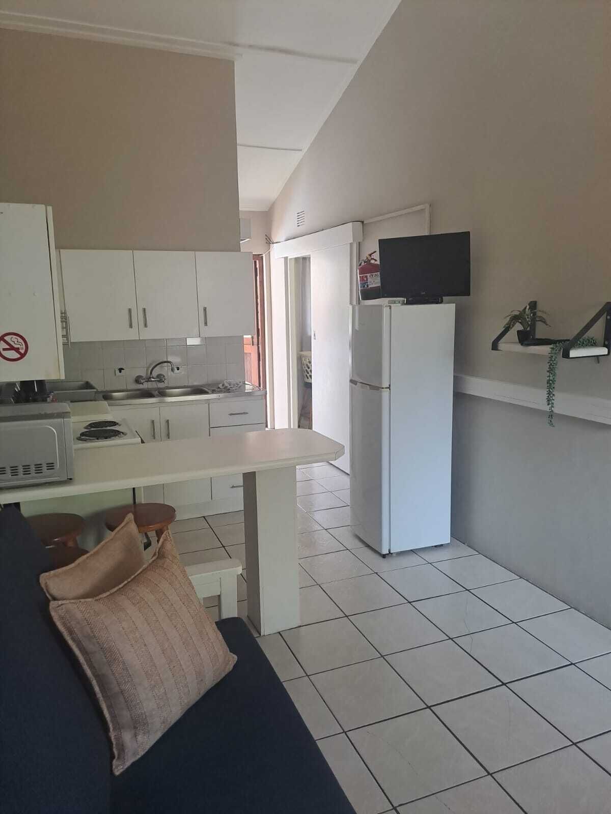 A compact kitchen with white cabinets, a refrigerator, a microwave, and a television mounted on the wall.