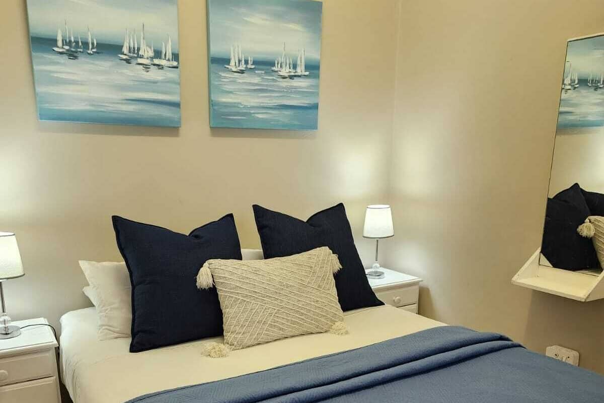 A neatly made bed with a blue bedspread and pillows, a bedside lamp, and a nightstand.
