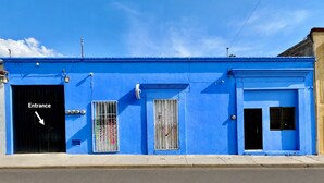 A blue building with a black entrance door, a window with a metal gate, and a small window with a curtain. - Hidden Gem: Bright and spacious apartment, just steps from Oaxaca’s best spots!  (Oaxaca de Juárez)
