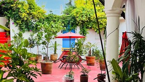 A courtyard with potted plants, a red umbrella, and a white building with a balcony. - Hidden Gem: Bright and spacious apartment, just steps from Oaxaca’s best spots!  (Oaxaca de Juárez)