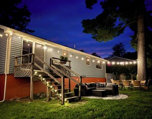 A two-story house with a covered porch, outdoor seating, and string lights.