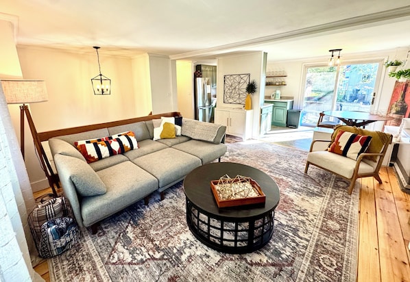 A living room with a sofa, a coffee table, and a chair. There is a kitchen in the background.
