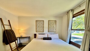 Camera d'albergo ordinata con un letto grande, un comodino con una lampada, pannelli decorativi e vista all'esterno attraverso una finestra.