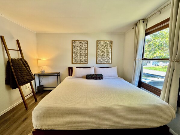 Ein ordentlich eingerichtetes Hotelzimmer mit einem großen Bett, einem Nachttisch mit Lampe, dekorativen Wandverkleidungen und Blick ins Freie durch ein Fenster.