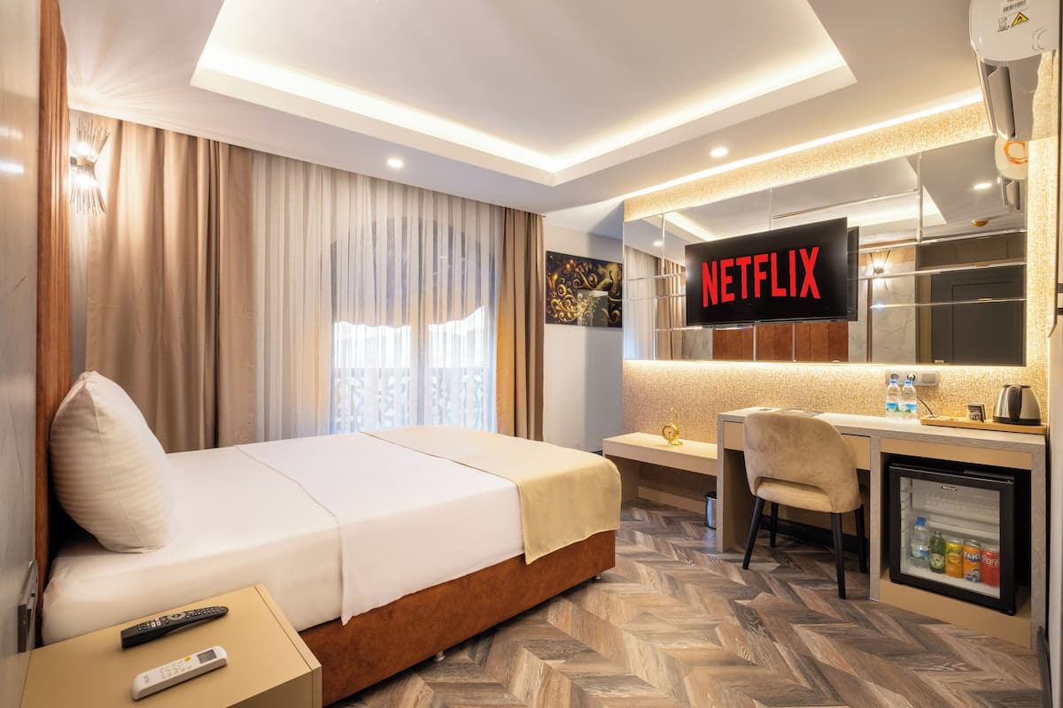 Quarto de hotel com cama, escrivaninha com cadeira, minibar e televisão exibindo "NETFLIX".