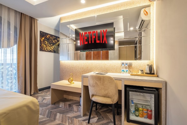 A hotel room with a minibar, a desk, a chair, a bed, a television displaying 'NETFLIX', and a small refrigerator. - 216 Star (Istanbul)