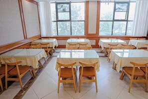 A dining area with multiple tables and chairs, large windows with curtains, and a tiled floor. - Vienna Classic Hotel (Xi'an Railway Station North Square Anyuanmen Metro Station) (Xi'an)