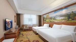 Ein Hotelzimmer mit zwei Betten, einem Schreibtisch mit einem Laptop, einem Stuhl und einem Bild an der Wand.