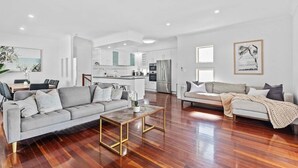 A spacious living room with a grey sofa, a coffee table, and a dining area with chairs and a table. - Manly Oasis 5BR - 3 King Beds, Pool, BBQ (Manly)