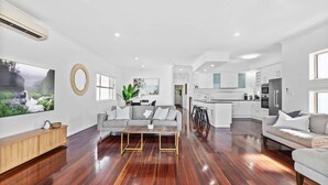 A spacious living area with a grey sofa, a coffee table, and a TV on the wall. - Manly Oasis 5BR - 3 King Beds, Pool, BBQ (Manly)
