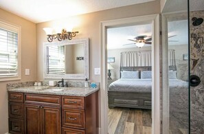 A bathroom with a granite countertop, wooden cabinets, a large mirror, and a ceiling fan. - Daytona Beach Shores House - walk to beach & restaurants (Daytona Beach)