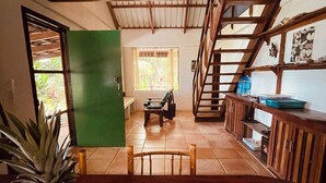 Une table de salle à manger en bois, sur laquelle se trouvent un ananas, une serviette enroulée et une chaise. Un escalier mène à un niveau supérieur.