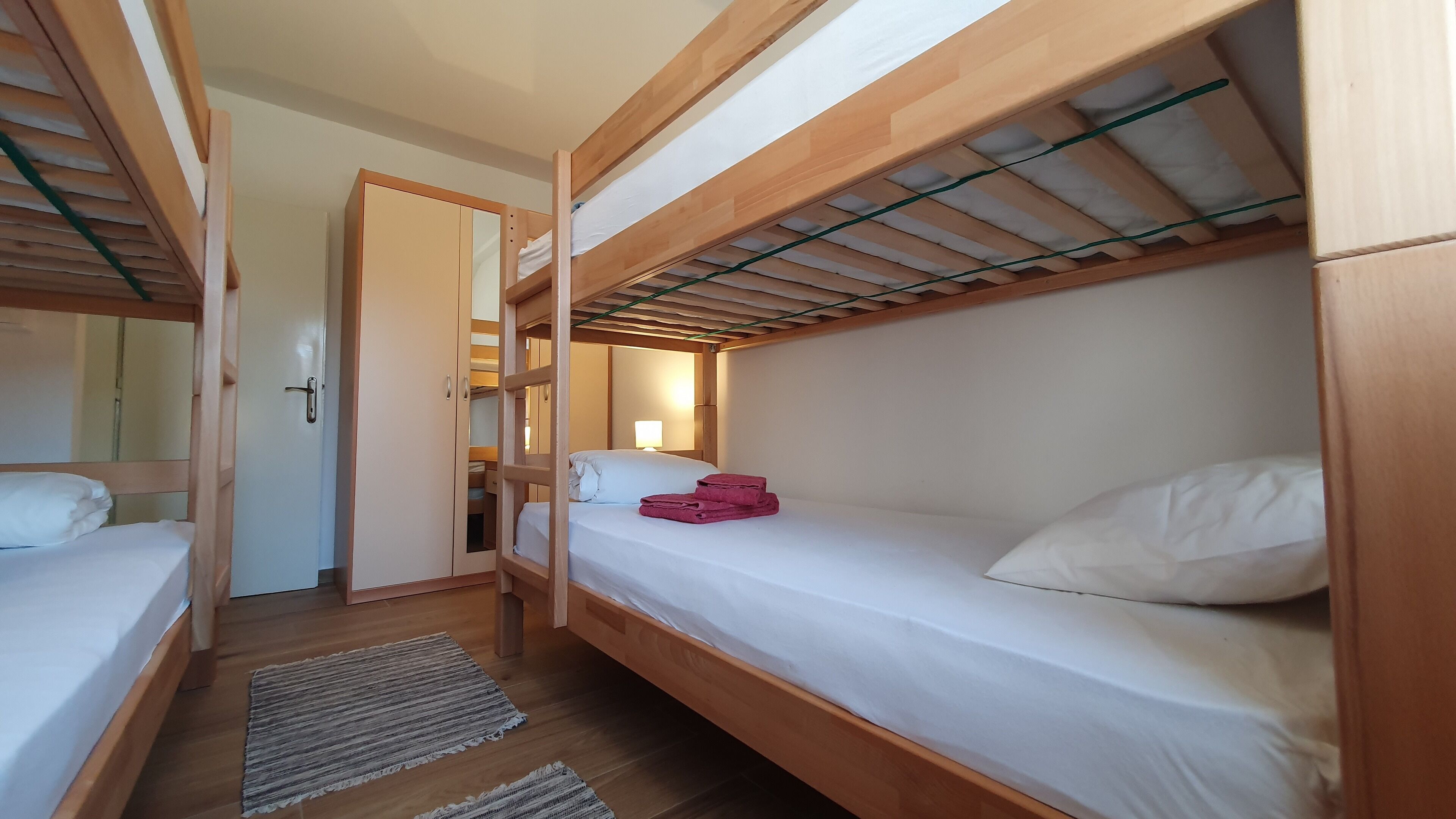 A compact hotel room with two wooden bunk beds, a small walk-in closet, and a bedside lamp.