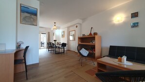 A modern living room with a wooden floor, a black sofa, a dining area with chairs, and a black chair with a cushion.