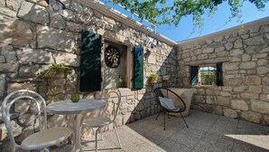 A stone building with a dartboard and a clock on the wall, a table with chairs, and a window with a view.