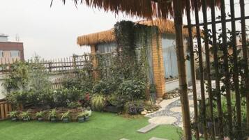 A rooftop garden with a thatched-roof structure, potted plants, and a small pathway.