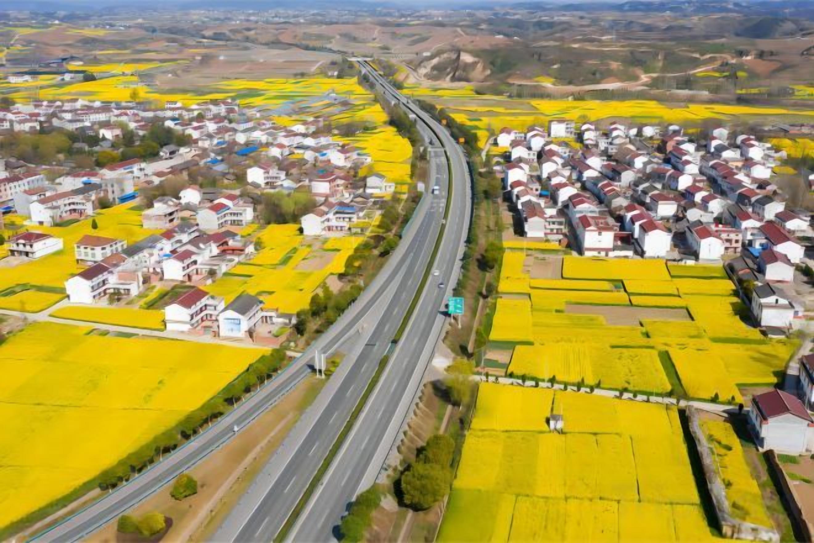 Une zone rurale traversée par une route, entourée de champs et de maisons.