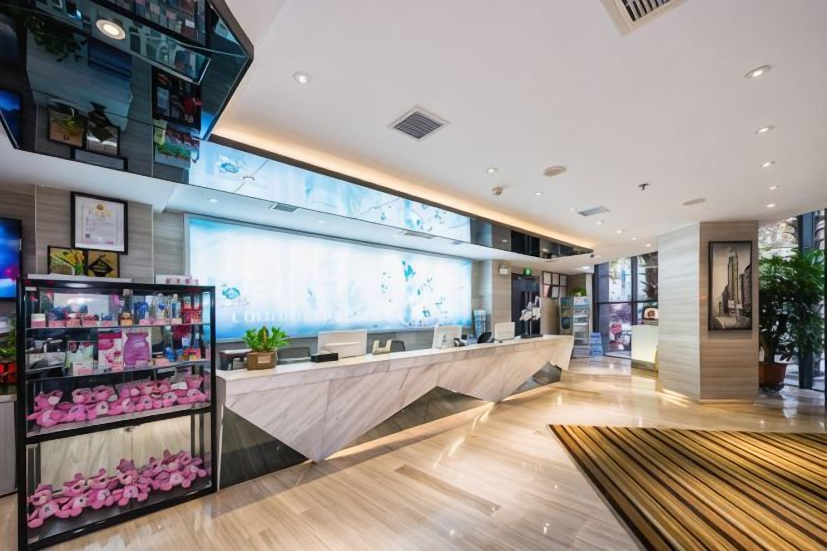 A modern hotel lobby with a reception desk, a plant, and a display of pink items.