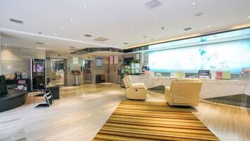 A modern lobby with a reception desk, seating area, and a large digital display.