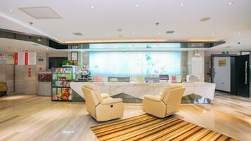 A hotel reception area with a reception desk, two armchairs, a patterned rug, and a counter with various items.