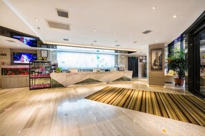 Un hall d’hôtel moderne avec un comptoir d’accueil, un téléviseur et une grande fenêtre.