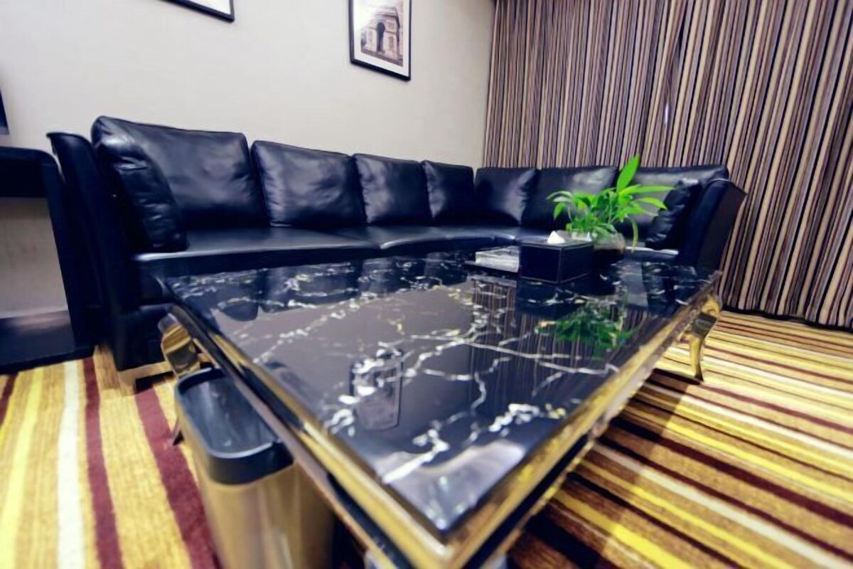 A black leather sofa with a glass coffee table in a room with striped carpet and a striped curtain.