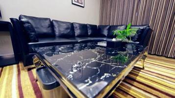 A black leather sofa with a glass coffee table in a room with striped carpet and a striped curtain.