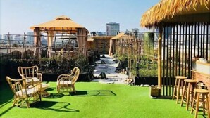Μια ταράτσα με τεχνητό χλοοτάπητα, έπιπλα από μπαμπού, ένα μικρό καταρράκτη και μια κατασκευή με στέγη από καλάμια.