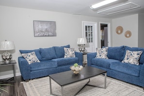 A living room with two blue sofas, a coffee table, and a painting on the wall. - Modern 4BR Home - Very Spacious - Minutes from Georgia International Horse Park (Conyers)