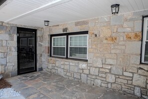 A stone exterior with a covered porch, a glass door, and two windows with black frames. - Modern 4BR Home - Very Spacious - Minutes from Georgia International Horse Park (Conyers)