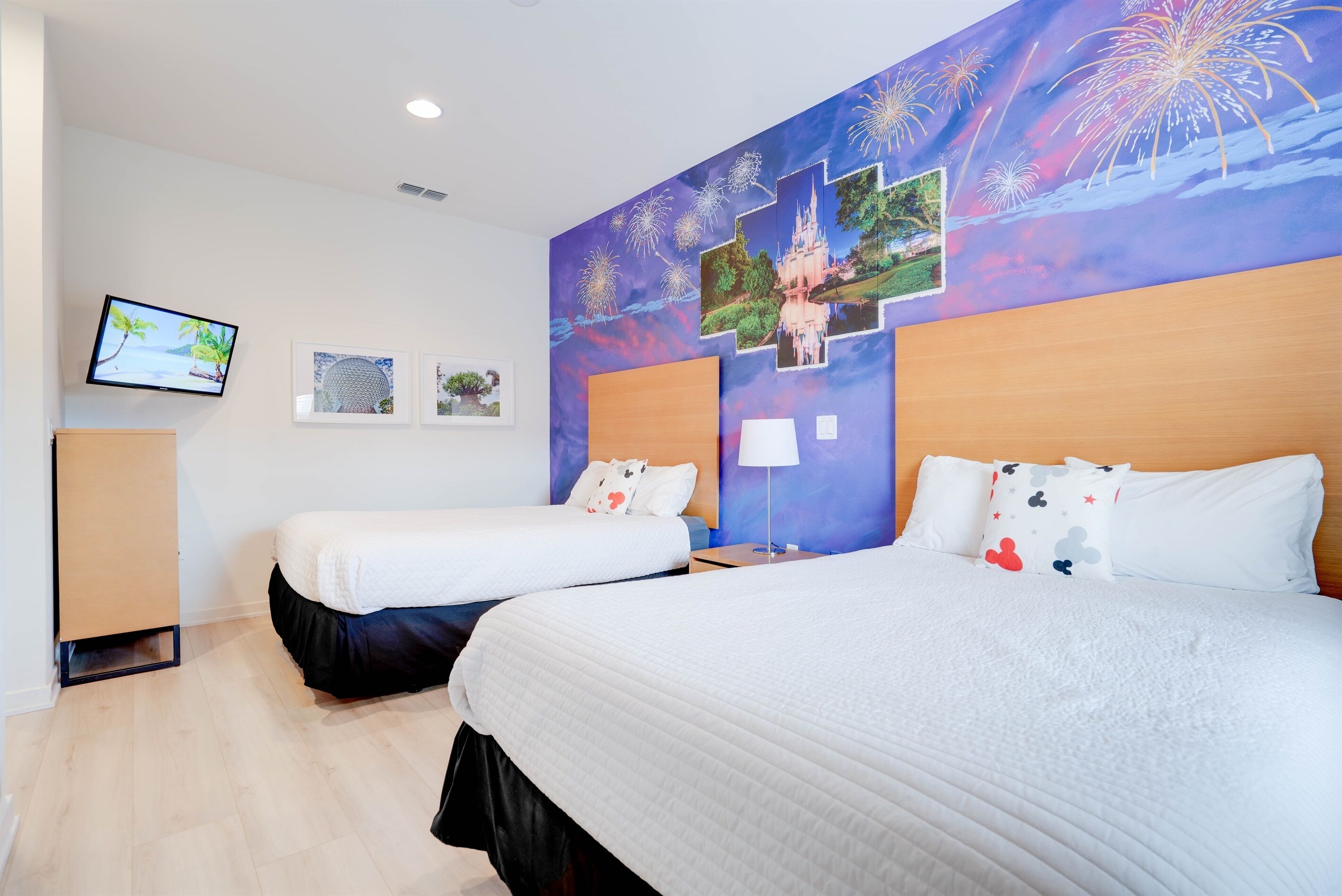 A hotel room with two beds, a television, and a wall decorated with fireworks and pictures.