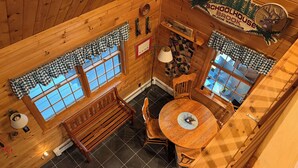 L’intérieur d’une cabane avec des murs en bois, une table ronde, un banc et une cheminée.