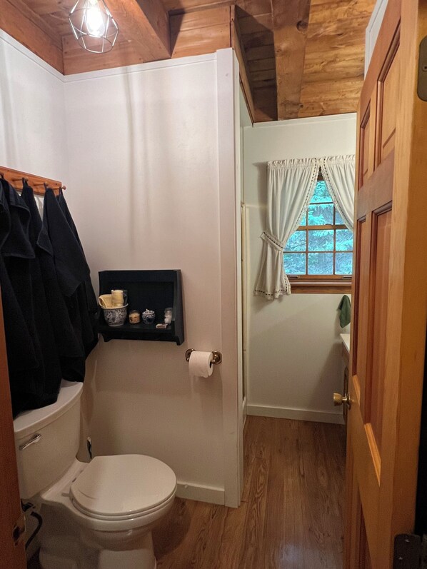 Een kleine badkamer met toilet, een plank met toiletartikelen en een raam met gordijnen.